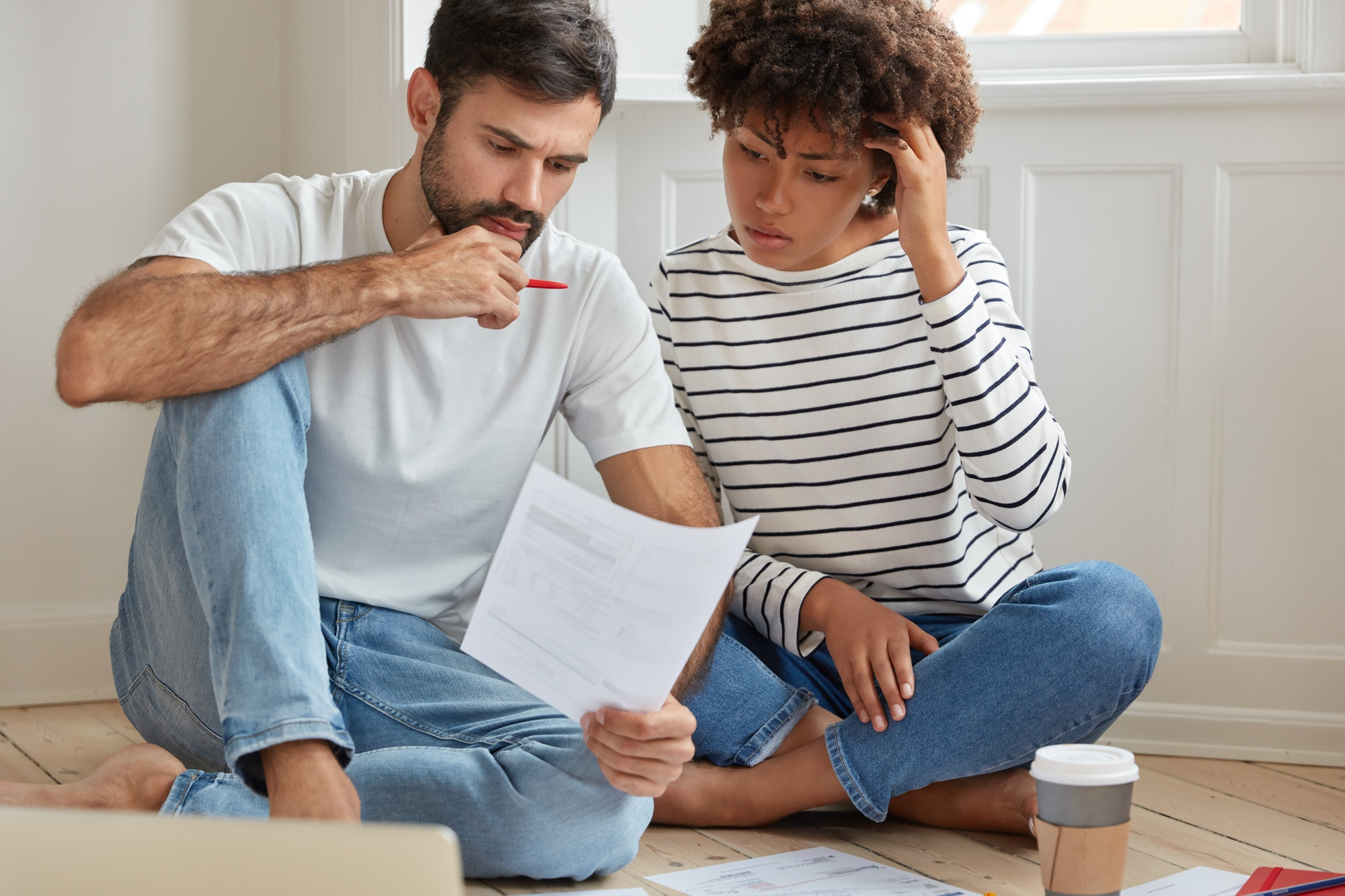 Couple reviewing financial documents at home, worried about expenses and bills