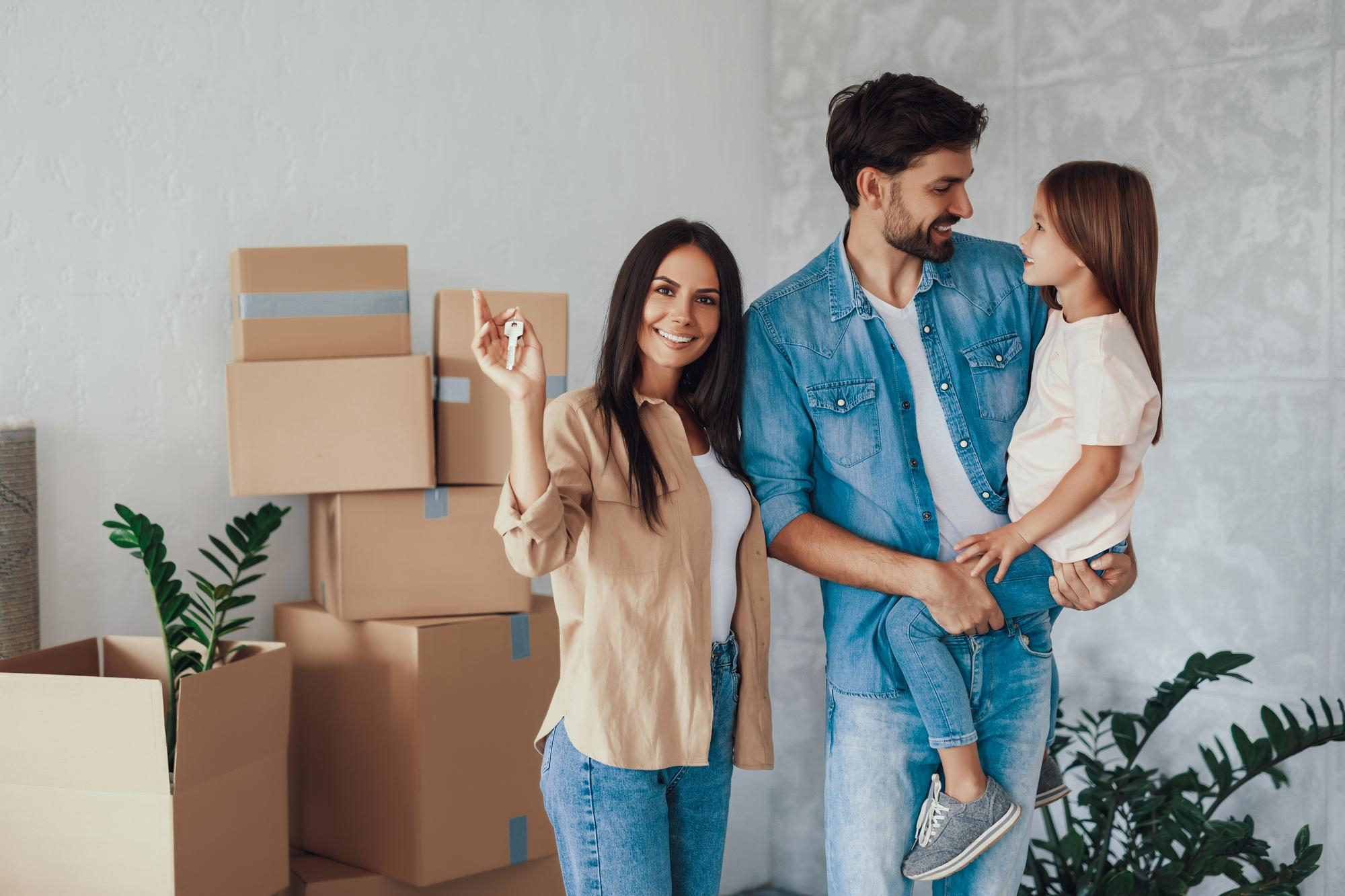 Happy family with moving boxes, mother holding new house keys, concept of home ownership.