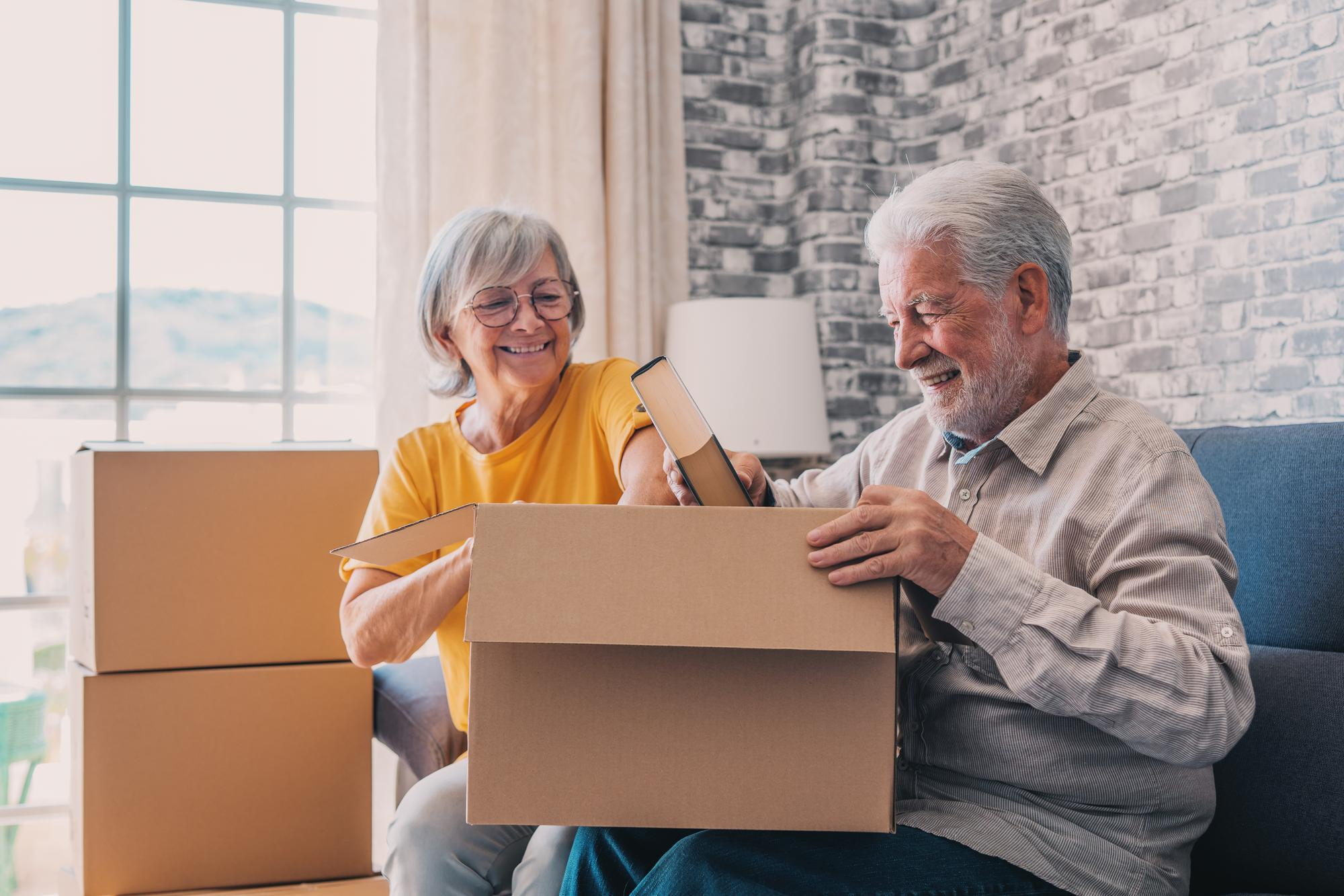 Happy senior couple unpacking moving boxes together at home, smiling and enjoying the transition after retirement.
